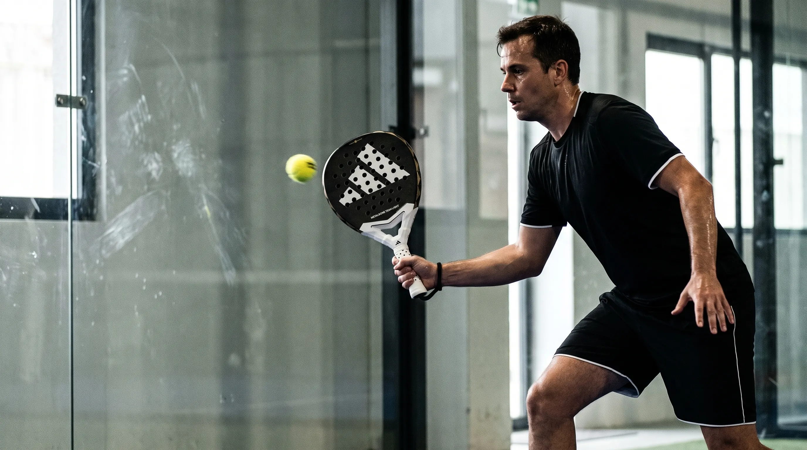 KI-generiert: Durch die Glaswand fotografiert: Spielerin spielt mit dem Adidas Metalbone Team Light 3.4 einen Ball nach dem Wandabpraller